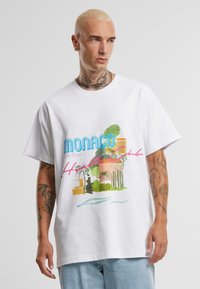 Biela bavlnená tričko s farebnou potlačou s nápisom "Monaco Côte d'Azur" a tropickými dizajnovými prvkami, vo voľnom strihu, s krátkymi rukávmi.