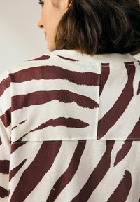 Braun- und cremefarbener gestreifter Shirt mit breiten Tigerstreifen, lockerer Passform, weichem Material und einer Nahtdetails auf der Rückseite.