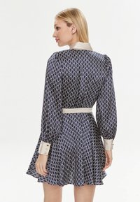 Abito blu navy con motivo bianco del logo, maniche lunghe a sbuffo, colletto e polsini crema, vita stretta e gonna svasata. Texture del tessuto liscia.