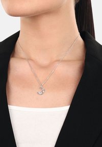 Collana d'argento con un pendente a forma di luna crescente, arricchita da due decorazioni, su una delicata catena, indossata su un collo nudo contro un blazer nero.