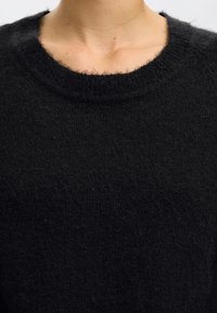 Camisola preta de malha com decote redondo, textura suave, superfície ligeiramente felpuda e corte descontraído. Sem padrões ou detalhes visíveis.