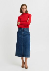 Rotes geripptes Langarmoberteil kombiniert mit einem blauen Jeans-Midirock. Das Rock verfügt über einen vorderen Schlitz und ein klassisches Fünf-Taschen-Design.