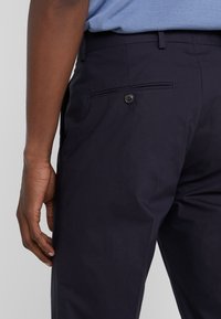 Marina byxor med en slät textur, med en bakficka med en enda svart knapp och skräddarsydd design.