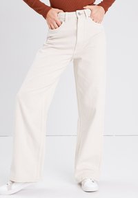 Bredde ben, cremefarvede jeans i denimstof med forlommer, høj talje og kontrastsyninger. Parret med hvide sneakers.