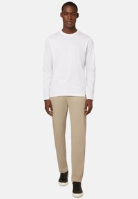 Valkoinen pitkähihaiset paita yhdistettynä beigeihin housuihin ja mustiin lenkkareihin. Ominaisuuksiin kuuluu pyöreä kaula-aukko ja rento istuvuus. Yksinkertainen muotoilu.