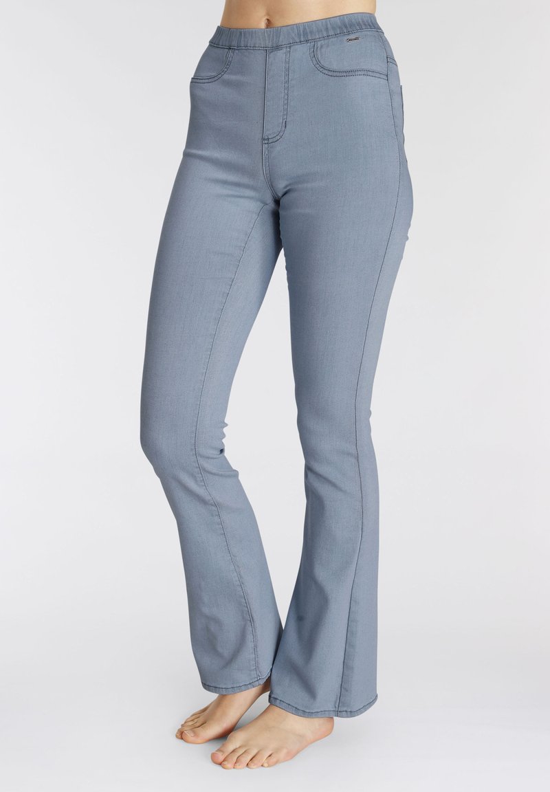 Blue denim flared pants feature a wide waistband, subtle stitching details, and a smooth texture, extending to a flared hem at the ankles.