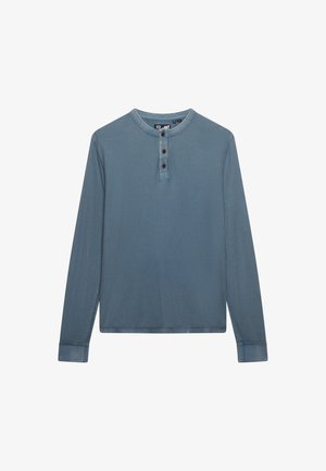 Niebieska koszula henley z długim rękawem, z trzema ciemnymi guzikami na przedniej plisce i okrągłym dekoltem.