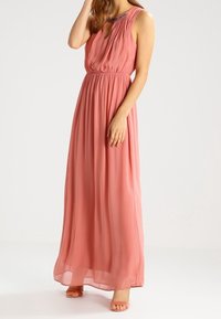 Abito maxi lungo senza maniche in un delicato rosa, caratterizzato da una scollatura arricciata e sottili dettagli in perline. Tessuto leggero e fluido.
