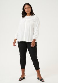 Valkoinen pitkähiha blouse, jossa on rypytysdetaljeita, nappisuljenta ja brodeerattuja yksityiskohtia, yhdistettynä mustiin slim-fit-housuihin ja mustiin korkoihin.