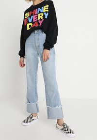 Black sweatshirt with colorful "SHINE EVERY DAY" text; light blue high-waisted jeans with frayed cuffs; black and white checkered slip-on shoes.