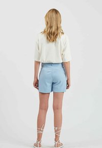 Shorts bleu clair à coupe ajustée, avec deux poches arrière et passants pour ceinture, associés à un haut blanc à coupe ample. Texture de tissu lisse.