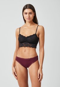Zwarte kant bralette met scalloped randen, gecombineerd met bordeauxrode hipster onderbroek met kanttrim. Beide stukken zijn benadrukt tegen een neutrale achtergrond.