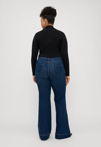 Jeans évasés bleu marine avec une taille mi-haute, dotés de deux poches arrière et de surpiqûres visibles, assortis à un haut à manches longues noir.