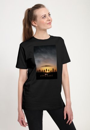 Zwarte t-shirt met een grafische print die een silhouet van een zonsondergang weergeeft met figuren en de tekst "ETERNALS" onderaan. Casual fit, korte mouwen.