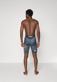 Pantaloni corti da performance a motivo nero e grigio con logo Venum sulla cintura. Design aderente, taglio alla lunghezza del ginocchio, texture liscia.