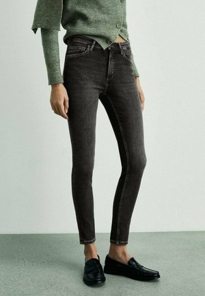Jeans skinny neri in denim con una texture liscia, dotati di vita media e dettagli di cuciture sottili. Abbinati a mocassini neri.