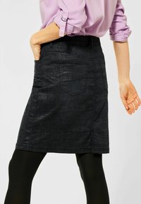Černá džínsová sukně s texturovaným povrchem, ke kolenům, s dvěma zadními kapsami a slim fit střihem. Nosená s černými punčochami.