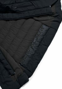 Giacca nera isolata con una texture trapuntata, con cerniere e marchio discreto all'interno. Presenta un taglio moderno e affusolato.