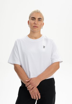 Weißes Baumwoll-T-Shirt mit kurzen Ärmeln und einem runden Halsausschnitt, das ein kleines schwarzes gesticktes Logo auf der linken Brustseite zeigt.