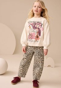 White sweatshirt with colorful horse graphic and “TRUE kindness” text, paired with beige leopard print pants and burgundy shoes.