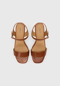Brune lær sandaler med hæl og brede frontremme, ankelrem med spænde, glat tekstur og firkantet tådesign. Merket "ANNA FIELD."