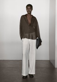 Brun gennemskinnelig skjorte med knapper og brede ærmer, parret med løstsiddende lysegrå linnedbukser. Accessorized med en sort tekstureret clutch.