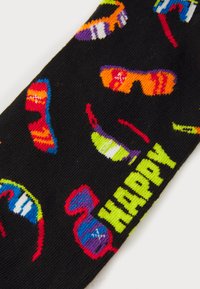 Μαύρη κάλτσα με πολύχρωμα σχέδια από γυαλιά ηλίου. Το κείμενο γράφει "ΧΑΡΟΥΜΕΝΟΣ" με έντονο πράσινο χρώμα. Μαλακή υφή με ζωντανά πολύχρωμα κεντήματα.