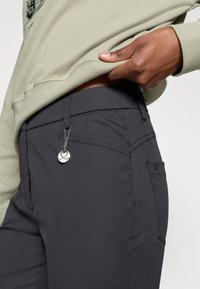 Melni bikses ar gludu tekstūru, kurām ir sānu kabata un sudraba piekariņš, kas piestiprināts pie ķēdes. Apvienotas ar gaiši zaļu sporta jaku.