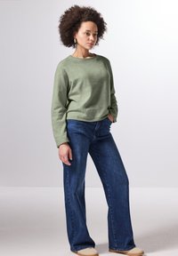 Grüner, leichter Sweatshirt mit Rundhalsausschnitt und langen Ärmeln, kombiniert mit weit geschnittenen, dunkelblauen Jeans. Lässiger, lockerer Schnitt und Textur.
