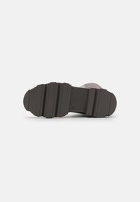 Zapatillas deportivas con una suela de goma negra texturizada que presenta ranuras profundas para proporcionar tracción, diseñadas para ofrecer estabilidad y agarre durante actividades al aire libre.
