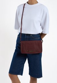 Bordeaux leren schoudertas met een gladde textuur, subtiele hardwareaccenten en een slanke, rechthoekige vorm. Kenmerkt zich door een geweven detail aan de voorkant.