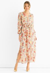 Floral maxi dress with a V-neckline, long puff sleeves, and a waist tie. Features a yellow-based fabric with red, blue, and green floral patterns.