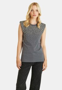 Gray sleeveless t-shirt with rounded neckline and studded embellishments on shoulders and upper front. Pair with black textured pants.