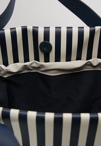 Sac fourre-tout rayé noir et crème avec intérieur en tissu noir et fermeture à bouton-pression, montrant une vue ouverte par le dessus avec des poignées.