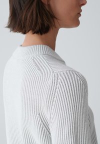 Hellgrauer Pullover mit gerippter Textur, runder Ausschnitt und horizontalen Streifen an den Schulternaht. Subtile Details.