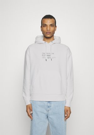 Felpa grigia chiara con tasca a marsupio frontale, cappuccio con cordino e stampa "CALVIN KLEIN EST 1968 NEW YORK, CITY". Tessuto morbido.