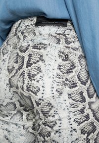 Jeans i slangeskinnsmönster i ljusgrått och svart, med en bakficka, en svart loggetikett och en slät textur.