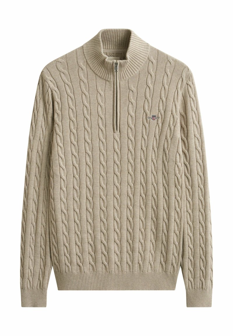 Pull en maille torsadée beige avec col, poignets et ourlet côtelés, doté d'une fermeture éclair sur un quart et d'un petit logo en forme de bouclier brodé sur la poitrine.