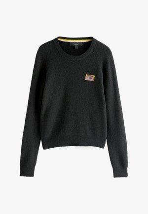 Melns kreklis, izgatavots no pūkainas materiāla, ar apaļu kakla izgriezumu, garām piedurknēm un krāsainu kasetes lentei līdzīgu izšuvumu priekšpusē.