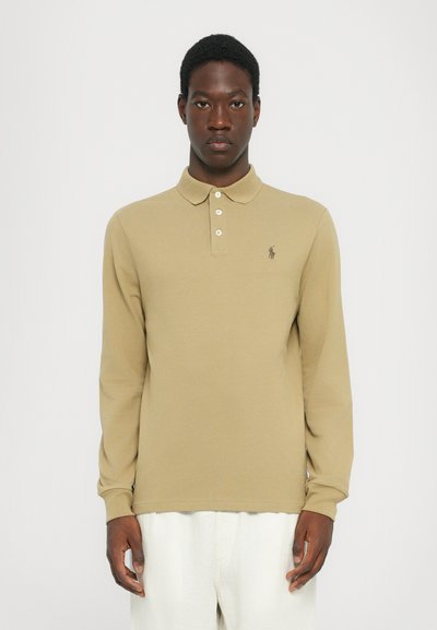Khaki polo tričko s dlouhým rukávem a límcem, tříknoflíkovou légou a malým vyšitým logem na levém prsním prostoru. Hladká textura.
