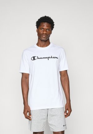 T-shirt blanc à manches courtes en coton, avec un logo "Champion" noir sur la poitrine ; associé à un short gris.