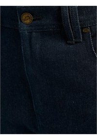 Dark blue denim trousers featuring a metal button closure, curved pocket seams, and a textured fabric surface.