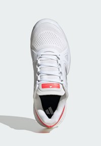 White athletic shoe with a breathable mesh upper, lace closure, black interior, and red accent on the tongue and heel. Features logo detail.