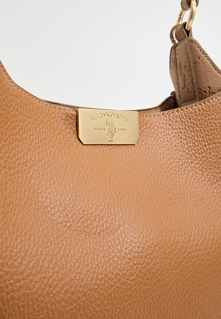 Tasche aus hellbraunem Leder mit strukturierter Oberfläche, ausgestattet mit einem goldfarbenen Metallschild. Runde Form mit gewölbtem Oberteil, verziert mit einer Kettenriemen.