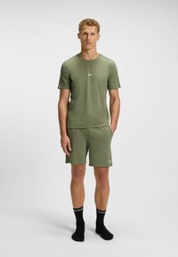 Olive green short-sleeved shirt and matching shorts. Made of smooth fabric with slight sheen. Branding on the front and shorts. Black socks with logo.