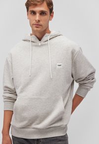 Light grey hoodie made of soft fabric, featuring a front pocket, adjustable drawstrings, and a small logo patch on the left chest.