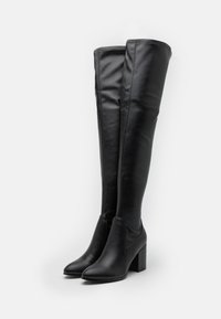 Botas de cuero negro hasta la rodilla con una textura suave, forma angular, tacón cuadrado y un sutil detalle de costura en los lados.