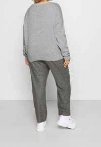 Pull en tricot gris clair avec une coupe ample et des épaules tombantes, associé à un pantalon texturé gris foncé et des baskets blanches.