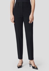 Czarne spodnie o dopasowanym kroju z prostymi nogawkami, wysokim stanem i kieszeniami bocznymi. Tkanina sprawia wrażenie gładkiej, o klasycznym, minimalistycznym stylu.