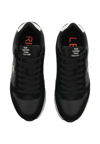 Un paio di scarpe da corsa nere con accenti bianchi, lacci neri e la scritta "CORRI PIÙ VELOCE DI QUANTO PUOI" sulla linguetta.